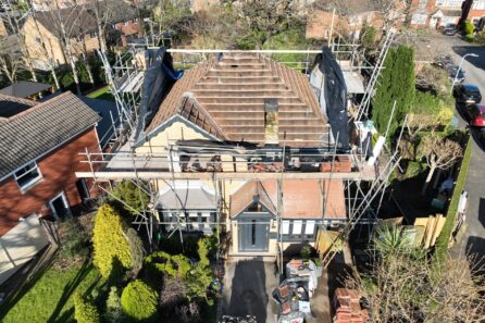 Scaffolding surrounding a residential building under roof renovation, with materials and tools visible on the ground.